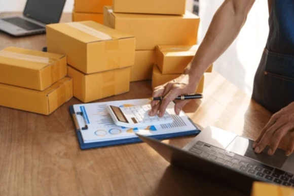 Person checking inventory numbers with a calculator and laptop in a Pacific Northwest business.